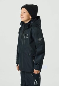 Black insulated jacket with two front pockets, zip closures, and branded accents. Worn with a matching black beanie.