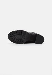 Suela de bota de goma negra con un patrón de banda de rodadura profundo y superficie texturizada, que presenta un ligero tacón y una marca grabada.