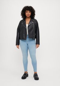 Black faux leather biker jacket with silver zippers, paired with light blue skinny jeans and chunky black shoes with studs.