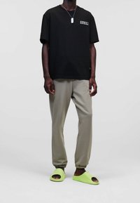 Černé oversized tričko s logem, béžové tapered kalhoty a jasně limetkové klouzavé sandály. Jednoduchý design, volný střih a jedinečné barvy.