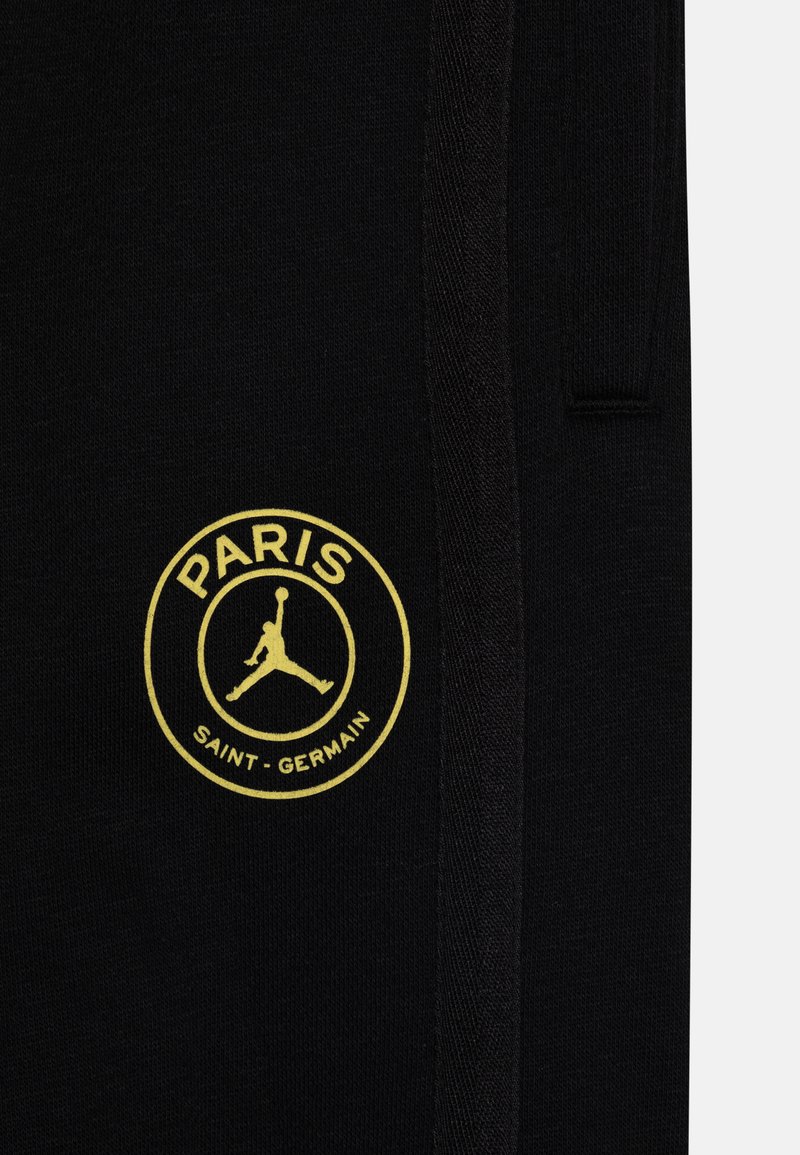 Czarne dresy z materiału z żółtym okrągłym logo z tekstem "PARIS" i "SAINT-GERMAIN", z designem skaczącej postaci na środku.