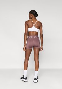 Λευκό σπορ σουτιέν με ρυθμιζόμενους ιμάντες, σε συνδυασμό με καφέ σορτς ψηλής μέσης που διαθέτουν ζώνη με λογότυπο. Μαύρα αθλητικά παπούτσια και λευκές κάλτσες.