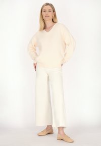 Maglione v-neck color pesco chiaro, vestibilità rilassata, abbinato a pantaloni bianchi a gamba larga e mocassini beige chiaro. Texture liscia, accenti minimi.