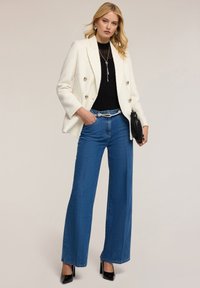 Valkoinen tweed-kaksirivinen bleiseri, musta ribattu toppi, leveälahkeiset siniset farkut, hopeinen vyö, musta laukkukotelo ja mustat korkokenkä.