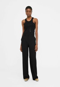 Top senza maniche nero con decorazioni, abbinato a pantaloni neri a vita alta. Vestibilità ampia con una superficie liscia. Scarpe dorate completano l'outfit.