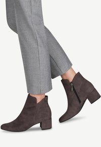 Botas de tobillo de ante gris con punta afilada, tacón bajo y cremallera lateral. Combinadas con pantalones cortos, de corte recto, en gris claro.