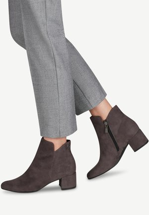 Bottes de cheville en suède gris avec un bout effilé, un petit talon carré et une fermeture éclair sur le côté. Associées à un pantalon taillé gris clair, coupé.