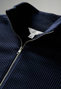 Pull en maille côtelée bleu marine, avec zip argenté, col montant et étiquette taille M "THE SET" à l'intérieur.
