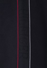 Tejido negro con un acabado texturizado, que presenta un sutil logotipo y rayas de acento en rojo y blanco a lo largo del costado.