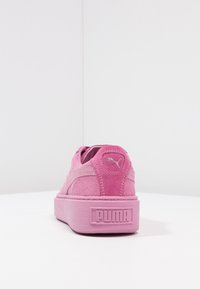 Sneaker en daim rose avec une semelle épaisse, présentant un talon surélevé et un petit logo argenté à l'arrière. Texture lisse et design minimaliste.