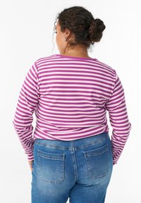 Duguljena majica s dugim rukavima u ljubičastim i bijelim prugama, rebraste teksture, okrugli izrez. Uparena s plavim trapericama visokog struka s stražnjim džepovima.