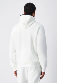 Felpa bianca con cappuccio e dettagli neri. Tessuto morbido e texture, caratterizzata da una vestibilità rilassata e polsini a costine. Branding minimale sul retro.