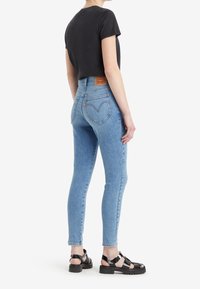 Jeans ajustados de color azul claro con una cintura alta, tejido de denim elástico y bolsillos traseros; combinados con una camiseta negra ajustada y sandalias negras.