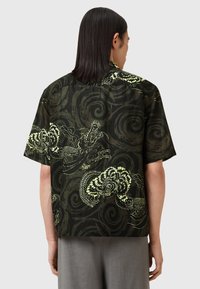 black short-sleeve shirt featuring an intricate green dragon and floral print against a dark swirling background, made of lightweight fabric.