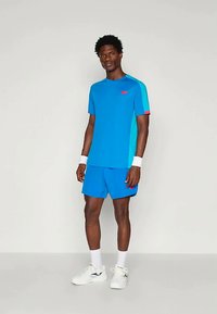 Μπλε αθλητικό σετ μπλούζας και σορτς, με αντίθετους μπλε και κόκκινους τόνους. Φτιαγμένο από ελαφρύ ύφασμα με λεπτή υφή.