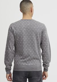 Pull gris avec un motif triangulaire blanc subtil, col rond à côtes et poignets côtelés, et coupe régulière. Le tissu semble doux avec une texture lisse.