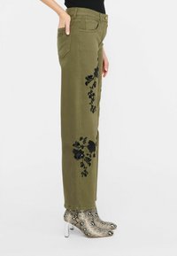 Olive roheline puuvillasegu püksid mustade lillemustritega külgedel; koos madala snake-print kingade ja läbipaistvate kontsadega.