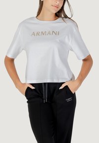 Witte gekorte t-shirt van katoen, met een gouden logo "ARMANI EXCHANGE" aan de voorkant, gecombineerd met zwarte joggers met zijzakken.