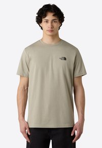 T-shirt a maniche corte in cotone leggera color khaki, con scollatura rotonda e un piccolo logo nero sulla parte superiore sinistra del petto.