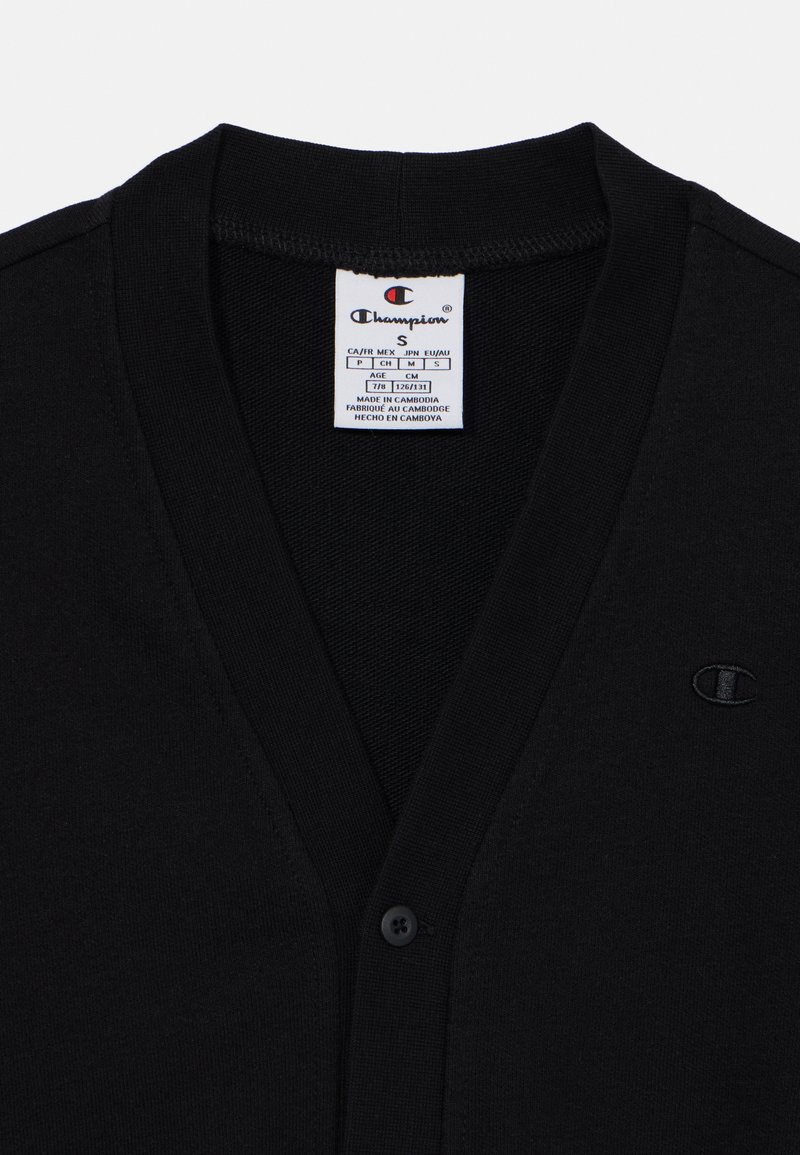 Cardigan nero in cotone, con scollo a V, chiusura frontale con bottoni e un piccolo logo ricamato sul lato sinistro. Etichetta della taglia visibile.