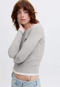 Gray long-sleeve shirt with a round neckline and white trim, paired with light blue high-waisted jeans, showing a side view and slight stretch.