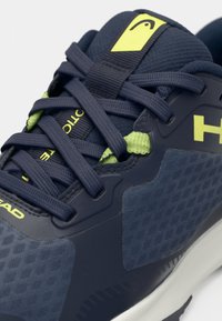 Jūras zila sporta kurpe ar acs un sintētiskiem materiāliem, ar spilgti dzelteniem akcentiem, teksturētām virsmas daļām un kontrastējošām šņorēm.