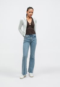 Ανοιχτό γκρι φούτερ με φερμουάρ, συνδυασμένο με εφαρμοστή σκούρα καφέ μπλούζα, μπλε παντελόνι με καμπάνα και λευκά αθλητικά, που παρουσιάζουν ένα casual σύνολο.