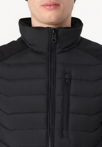 Black puffer jacket with a high collar, horizontal quilted pattern, zippered front, side zip pocket, and textured shoulder accents.