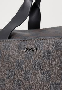 Brown patterned handbag made of textured faux leather, featuring smooth black handles and a metallic logo detail.