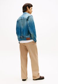 Τζιν μπουφάν σε ανοιχτό μπλε με άνετη εφαρμογή, που διαθέτει φιόγκο στο πίσω μέρος και καφέ δερμάτινο ταμπελάκι. Συνδυάζεται με μπεζ παντελόνια.