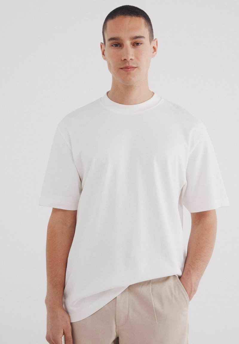 T-shirt bianca oversize con scollatura rotonda e maniche corte, realizzata in morbido cotone, abbinata a pantaloni beige.