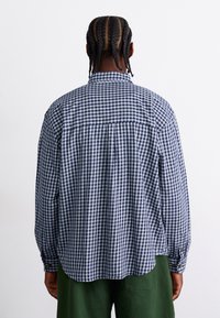 Camisa de manga larga a rayas en azul marino y blanco, fabricada en algodón, corte regular, yugo trasero, puños abotonados, dobladillo redondeado, superficie ligeramente texturizada.