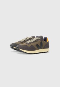 Sneakers sportivi in mesh verde oliva e grigio con dettagli neri. Presentano una suola beige, lacci grigi e un tassello sul tallone giallo a contrasto.