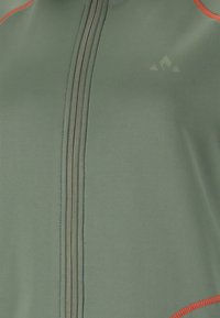 Grön sportjacka med orange detaljer, med hög krage, hel dragkedja, slät textur och en logotyp på bröstet.