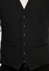Gilet formel noir à cinq boutons porté sur une chemise blanche, avec des poches avant et un ourlet pointu.