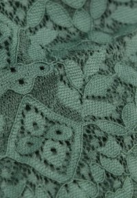 Groene gebreide stof met ingewikkelde kanten patronen met blad- en bloemmotieven, die de textuur en open weefsels door de hele stof benadrukt.