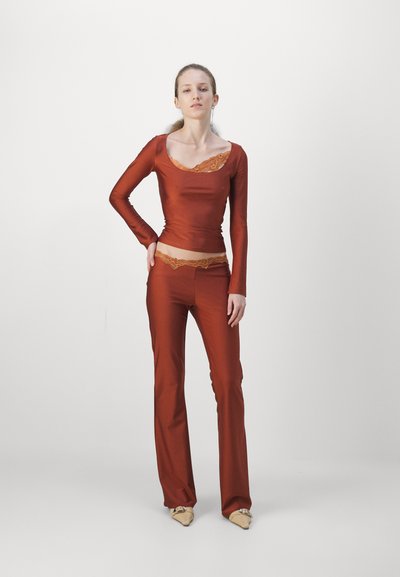 Top rosso a maniche lunghe con dettaglio in pizzo sul collo, abbinato a pantaloni aderenti coordinati. Tessuto morbido, vestibilità slim e un look coordinato.