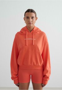 Oranje hoodie met een voorzak, trekkoorden bij de hals en geribde manchetten. Bijpassende oranje shorts met een getailleerd ontwerp.