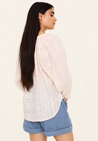 Light pink embroidered blouse with long, puffed sleeves and a rounded hem, paired with light blue rolled-up shorts.