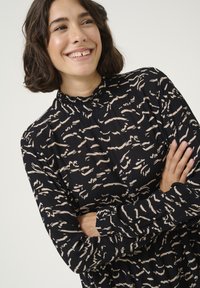 Robe noire à manches longues avec un col montant, présentant un motif abstrait crème, un col froncé et un tissu texturé.