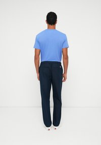 Kék, rövid ujjú póló sötétkék, rugalmas derekú nadrággal párosítva. A nadrág laza szabású, fehér cipőbe tűrve.