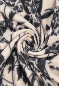 Motivo floreale nero su tessuto crema, trama testurizzata, arrotolato circolarmente, in mostra il design e i vari strati del tessuto.