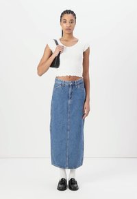 Gonna maxi in denim azzurro chiaro con vestibilità dritta, dotata di una cucitura frontale e passanti per cintura. Abbinata a un top corto bianco e scarpe nere.