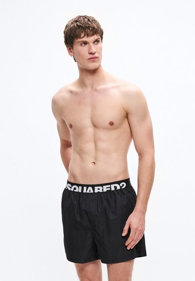 Bañador corto negro con cintura elástica que muestra texto de logo en blanco. Tejido ligero y suave con un diseño clásico de corte holgado.
