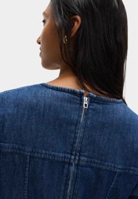 Mörkblå denimjacka med hög krage och dragkedjedetalj på baksidan. Har en strukturerad design och textilstruktur.