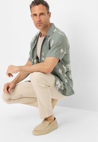 Short-sleeve green button-up shirt with floral pattern, cream t-shirt underneath, light beige linen pants, and beige slip-on shoes.