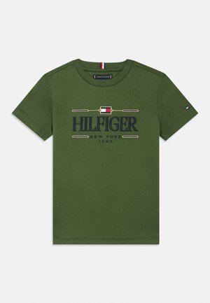 Olive green short-sleeve T-shirt with navy "HILFIGER NEW YORK 1985" text and a small red, white, and blue flag logo on the chest and sleeve.