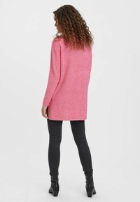 Vaaleanpunainen pitkä neuletakki, jossa on pehmeä rakenne, pitkähihaiset hihat ja suora leikkaus. Sitä on yhdistetty tummiin slim fit -farkkushortsit ja nilkkurit.