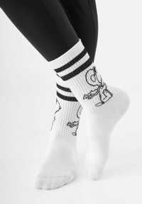 Weisse Crew-Socken mit schwarzen Streifen oben, mit einem cartoonhaften Charakterdesign in Schwarz an den Seiten. Rippstruktur.
