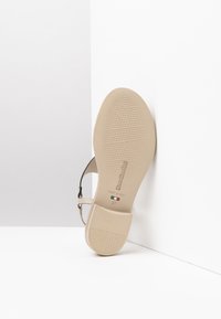 Sandale beige avec une semelle en caoutchouc texturée, bride ajustable et logo en relief. Taille 37, fabriquée en Italie. Vue de côté sur fond blanc.